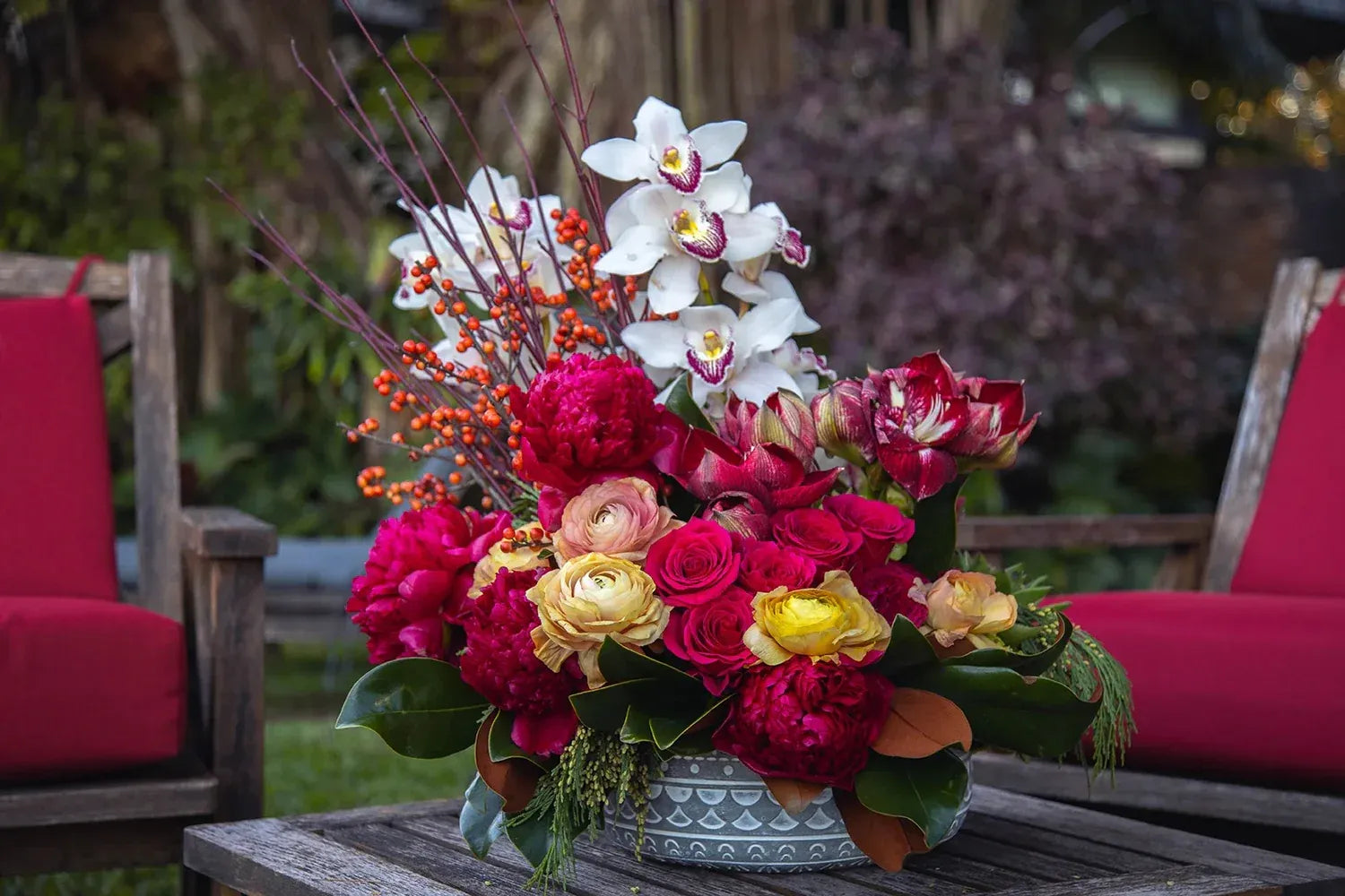 Vibrant floral arrangement featuring orchids, peonies, roses, and berries in a decorative bowl.