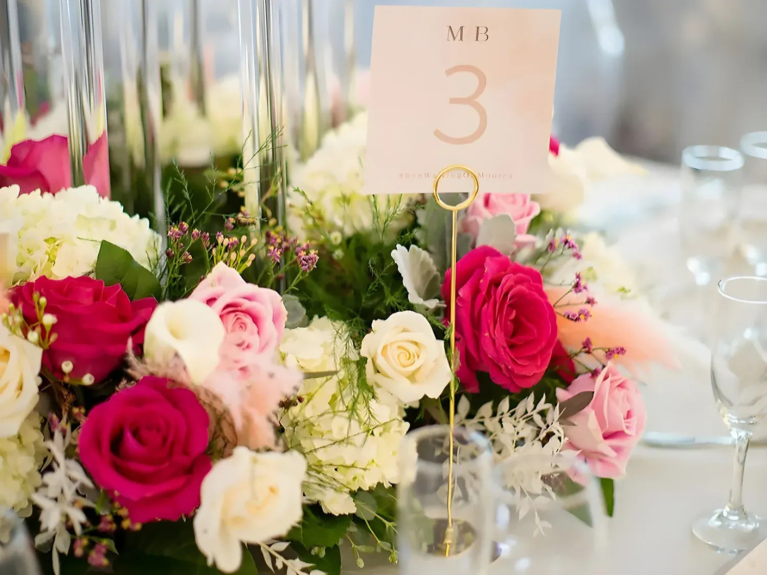 Elegant floral centerpiece with pink and white roses, adorned with a table number card. Perfect for events and weddings.