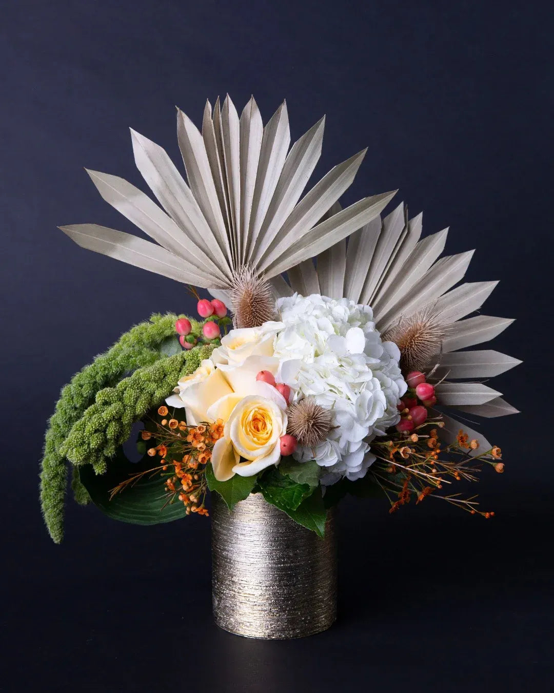 Elegant floral arrangement featuring white roses, hydrangeas, and textured greenery in a chic gold vase.