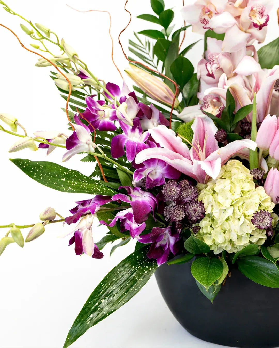 Vibrant floral arrangement featuring lilies, orchids, and greenery in a sleek black vase.