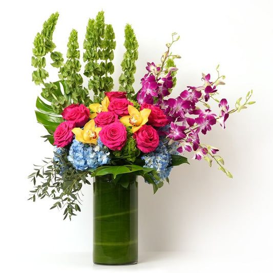 Vibrant floral arrangement featuring pink roses, blue hydrangeas, and purple orchids in a chic green vase.