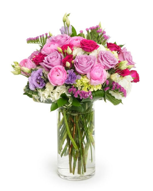 A vibrant bouquet of pink and purple roses, lisianthus, and garden flowers in a clear glass vase.