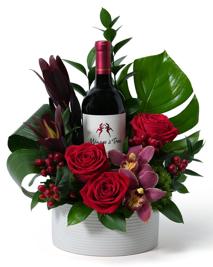 Elegant floral arrangement with red roses and an exquisite wine bottle, perfect for special celebrations.