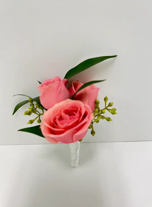 Elegant pink rose boutonnière with greenery, perfect for weddings or special events.