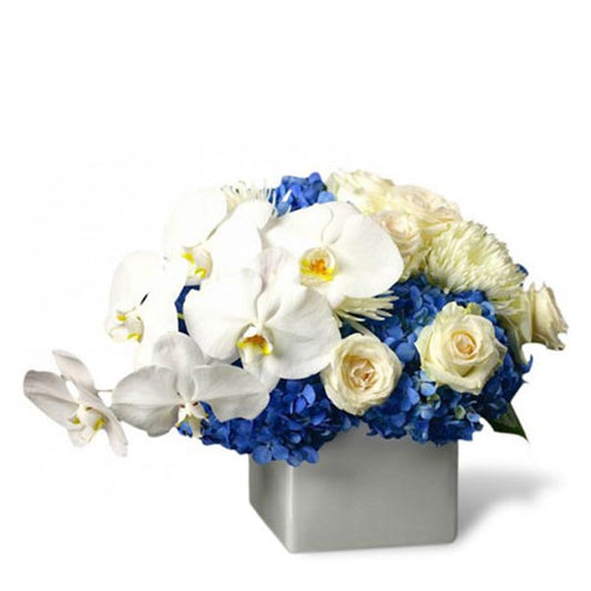 Elegant floral arrangement featuring white orchids, blue hydrangeas, and cream roses in a modern white vase.
